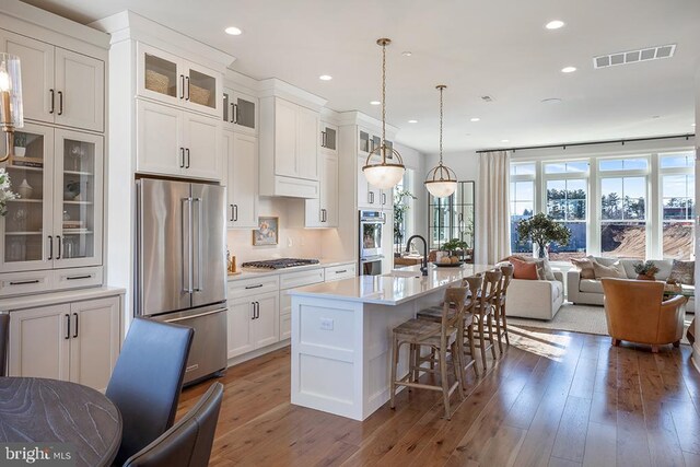 kitchen featuring a center island with sink, white cabinetry, stainless steel appliances, dark hardwood / wood-style floors, and a kitchen bar