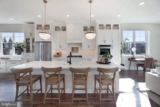 kitchen featuring decorative light fixtures, a kitchen island with sink, appliances with stainless steel finishes, and white cabinets