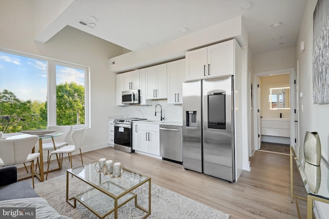 kitchen with decorative backsplash, white cabinetry, stainless steel appliances, and light hardwood / wood-style flooring