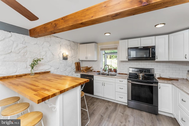 kitchen with black appliances, butcher block countertops, a kitchen bar, and white cabinets