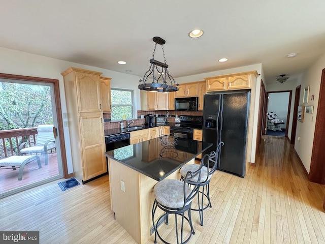 kitchen with a center island, black appliances, sink, decorative light fixtures, and light hardwood / wood-style floors