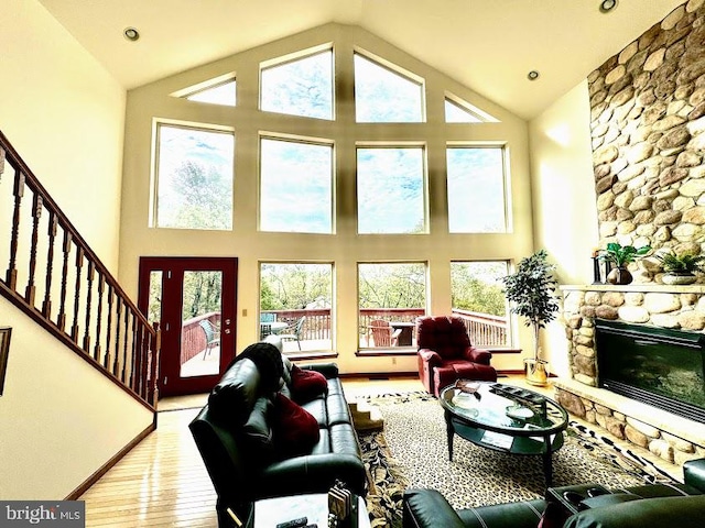 living room with a stone fireplace, light wood-type flooring, and high vaulted ceiling