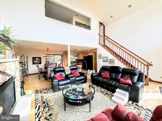 living room featuring a notable chandelier, light wood-type flooring, a fireplace, and high vaulted ceiling