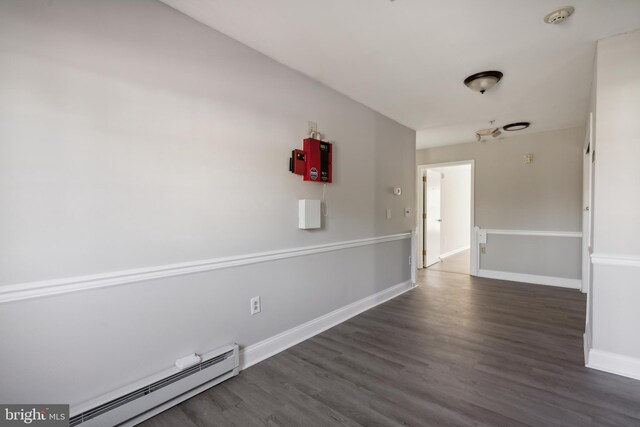 spare room featuring baseboard heating and dark hardwood / wood-style flooring