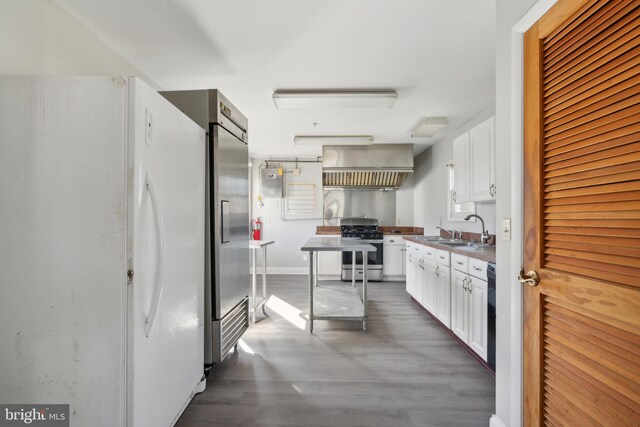 kitchen featuring wall chimney range hood, hardwood / wood-style floors, sink, stainless steel appliances, and white cabinetry