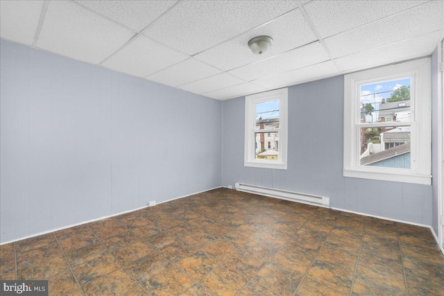 empty room with dark tile patterned flooring, a paneled ceiling, and a baseboard heating unit