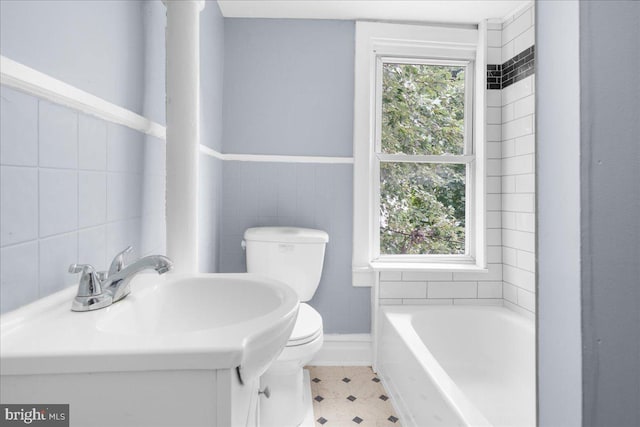 bathroom with a tub to relax in, a wealth of natural light, tile walls, and toilet