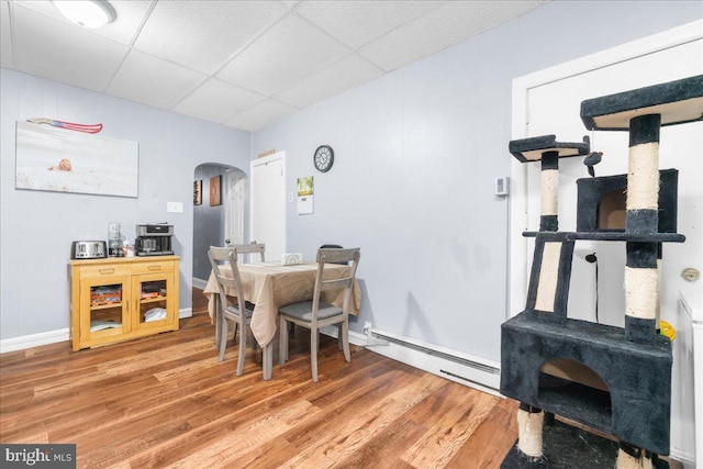 dining space with a paneled ceiling, baseboard heating, and hardwood / wood-style floors