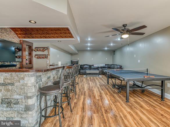 recreation room featuring bar area, light hardwood / wood-style flooring, and ceiling fan