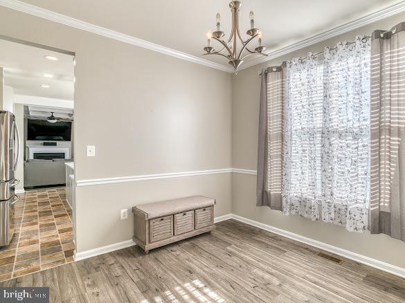 spare room with hardwood / wood-style floors, ceiling fan with notable chandelier, and ornamental molding