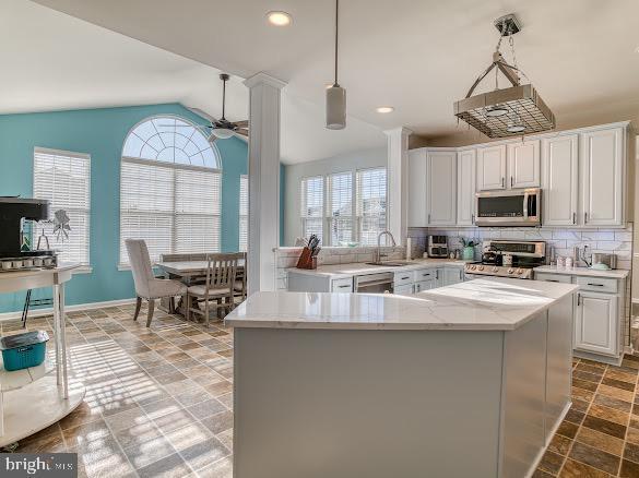 kitchen with decorative backsplash, stainless steel appliances, vaulted ceiling, white cabinetry, and hanging light fixtures