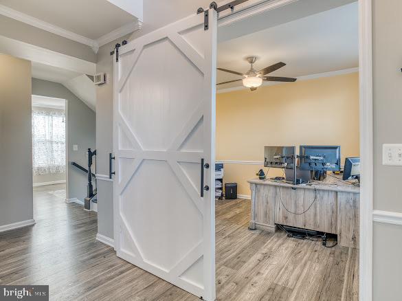 office area featuring ceiling fan, a barn door, wood-type flooring, and crown molding