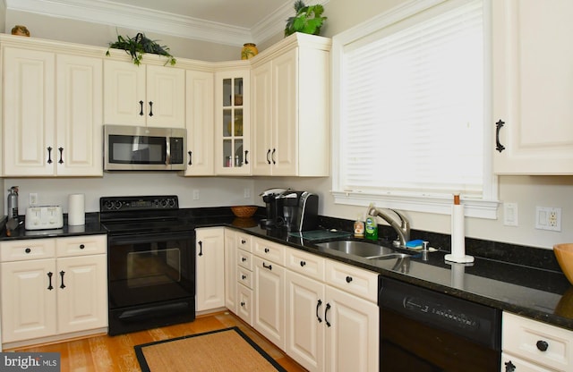 kitchen with sink, ornamental molding, black appliances, dark stone counters, and light wood-type flooring