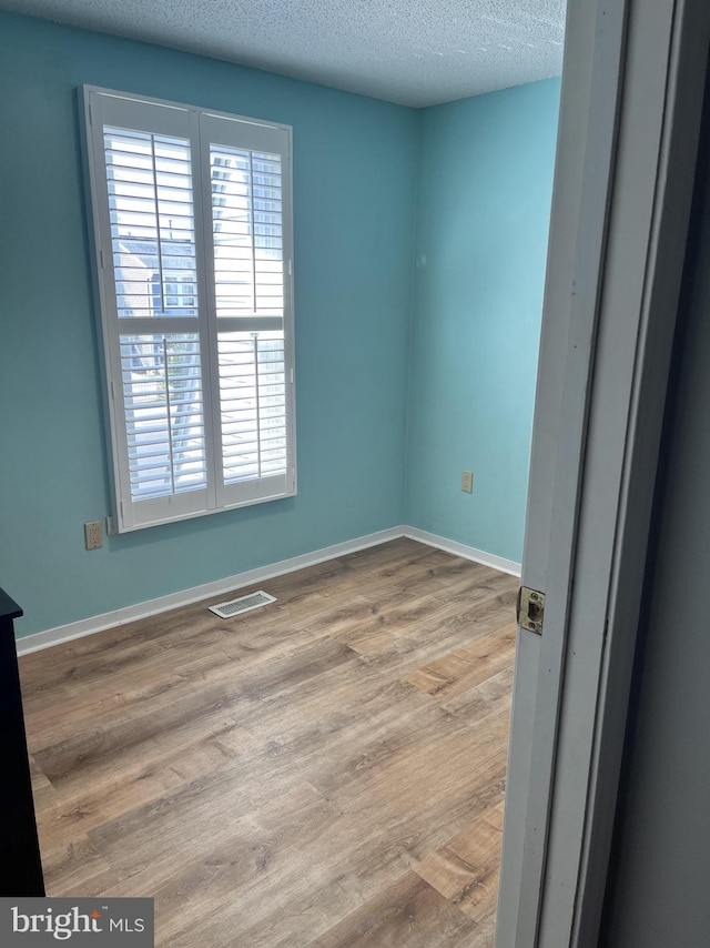 unfurnished room with light wood-type flooring and a textured ceiling