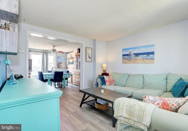 living room with ceiling fan, light hardwood / wood-style flooring, and a textured ceiling