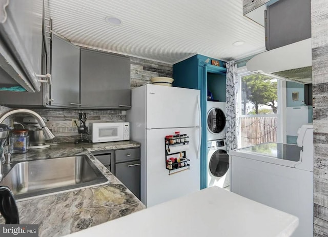 kitchen with sink, white appliances, gray cabinetry, stacked washer and clothes dryer, and decorative backsplash