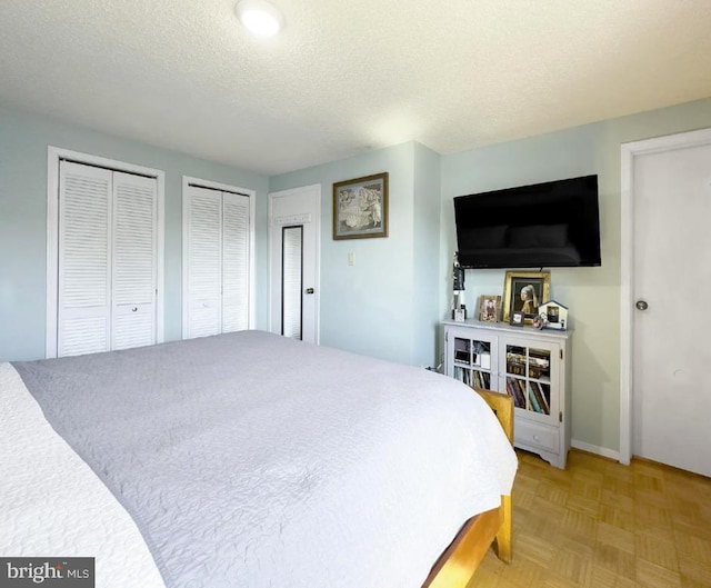 bedroom featuring a textured ceiling, two closets, and parquet floors