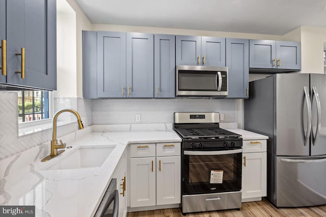 kitchen with appliances with stainless steel finishes, sink, light hardwood / wood-style floors, light stone counters, and decorative backsplash