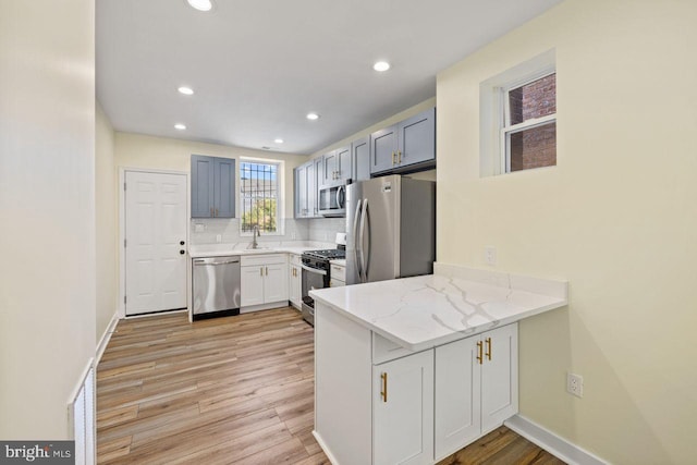 kitchen featuring light hardwood / wood-style floors, kitchen peninsula, light stone countertops, and stainless steel appliances