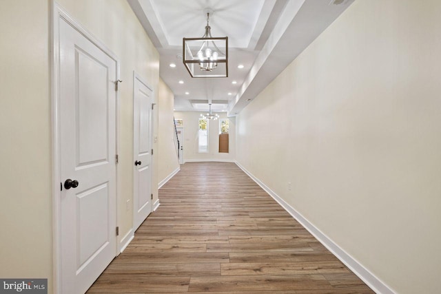 corridor with an inviting chandelier, light hardwood / wood-style floors, and a raised ceiling