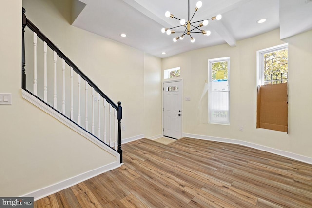 foyer entrance with light hardwood / wood-style floors, a notable chandelier, and beam ceiling