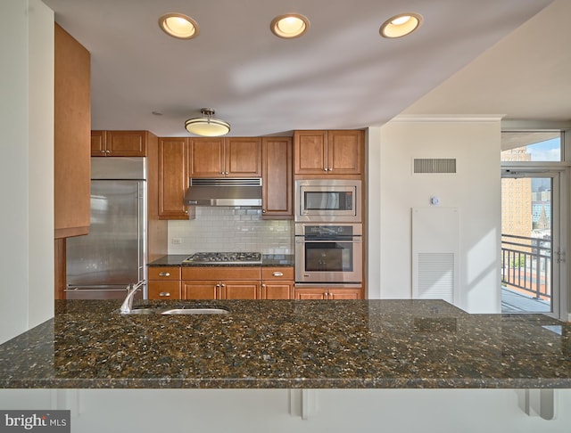 kitchen featuring tasteful backsplash, kitchen peninsula, built in appliances, dark stone countertops, and a breakfast bar