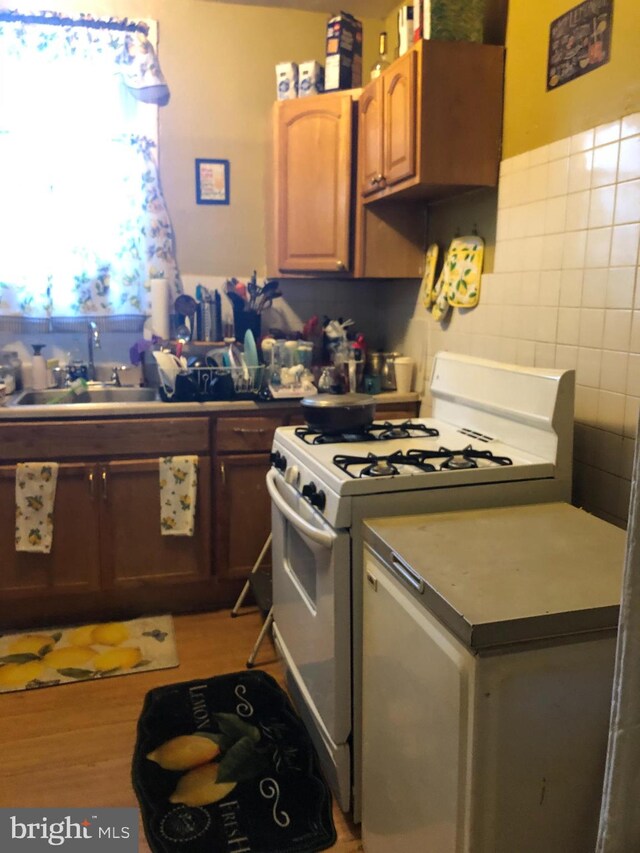 kitchen featuring white range with gas stovetop, sink, tile walls, and light hardwood / wood-style flooring