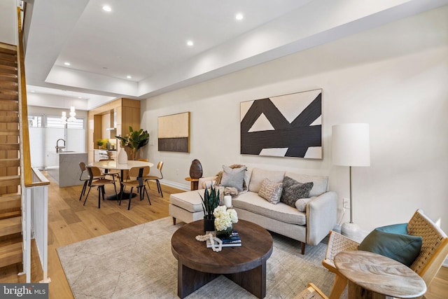 living room with sink, light hardwood / wood-style flooring, a tray ceiling, and an inviting chandelier