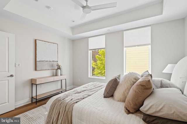 bedroom with a ceiling fan, a raised ceiling, baseboards, and wood finished floors