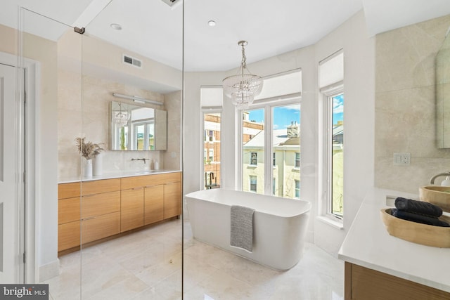 bathroom with a notable chandelier, tile walls, visible vents, vanity, and a freestanding tub