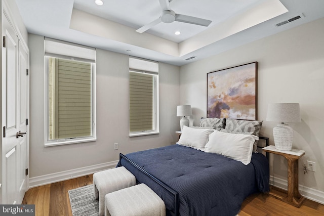 bedroom with ceiling fan, a raised ceiling, and wood-type flooring