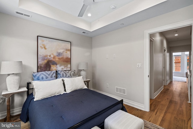 bedroom with dark wood-style floors, a raised ceiling, and visible vents