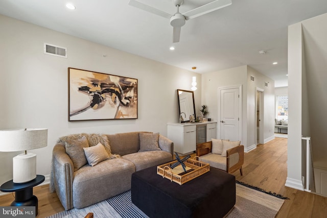 living room featuring ceiling fan, sink, and light wood-type flooring