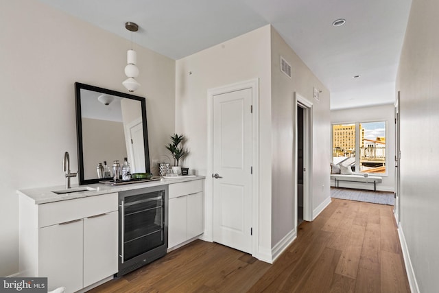 bar featuring beverage cooler, sink, hanging light fixtures, white cabinets, and dark wood-type flooring