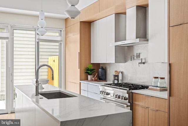 kitchen with wall chimney range hood, white cabinets, light stone countertops, high end stainless steel range, and sink