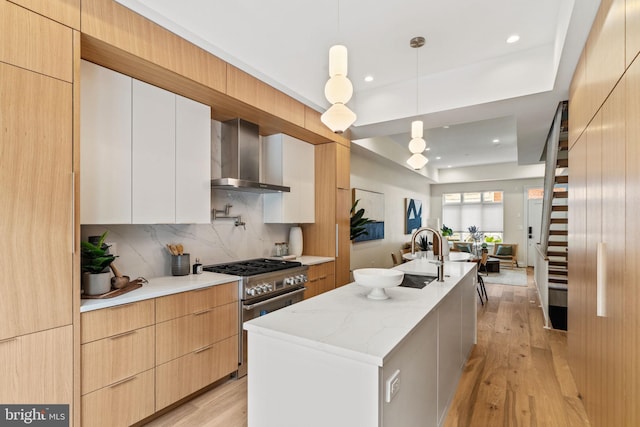 kitchen with decorative light fixtures, high end stainless steel range oven, wall chimney exhaust hood, modern cabinets, and a center island with sink