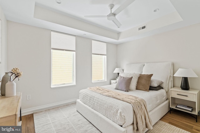 bedroom with wood-type flooring, a tray ceiling, and ceiling fan