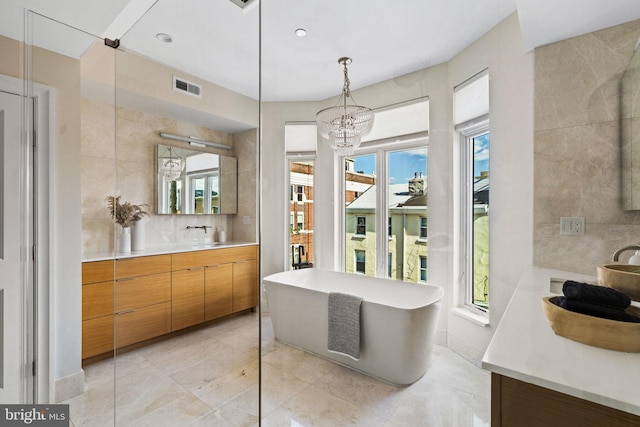 bathroom featuring a tub to relax in, vanity, tile walls, and an inviting chandelier