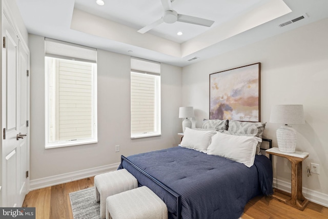 bedroom with a raised ceiling, ceiling fan, and light wood-type flooring