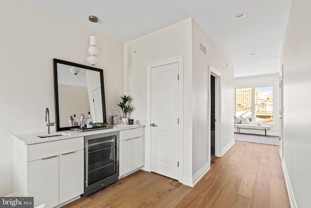 bar featuring sink, light wood-type flooring, decorative light fixtures, white cabinetry, and beverage cooler