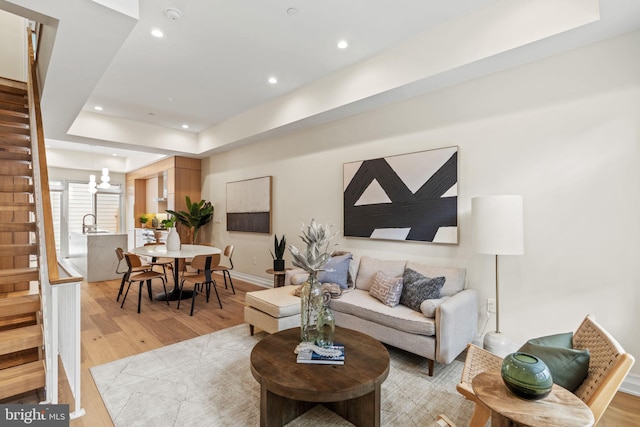 living room with a notable chandelier, sink, a tray ceiling, and light hardwood / wood-style flooring