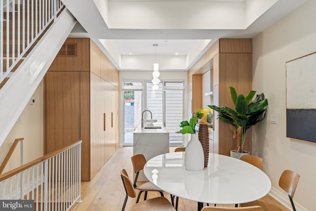 dining space featuring wood walls, light hardwood / wood-style floors, sink, and a tray ceiling