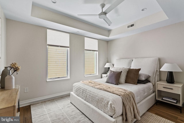 bedroom with hardwood / wood-style flooring, ceiling fan, and a tray ceiling