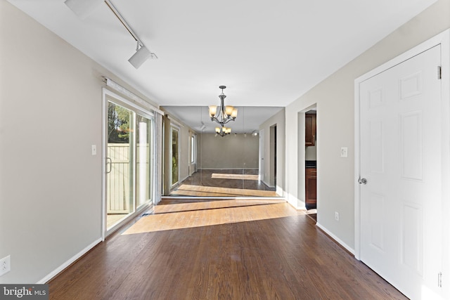 hallway featuring dark hardwood / wood-style floors, an inviting chandelier, and track lighting