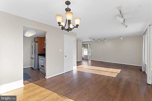 unfurnished living room with dark wood-type flooring, an inviting chandelier, and track lighting