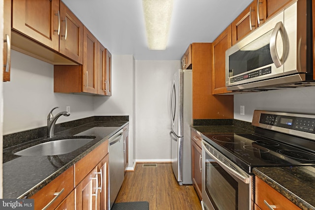 kitchen with appliances with stainless steel finishes, light wood-type flooring, dark stone counters, and sink