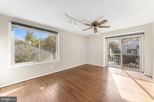 spare room with track lighting, hardwood / wood-style floors, a wealth of natural light, and ceiling fan