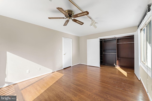 unfurnished bedroom with ceiling fan, track lighting, a closet, and hardwood / wood-style floors