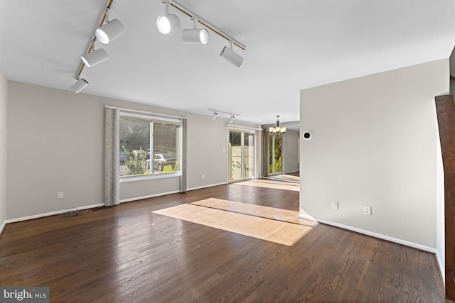 spare room with track lighting, dark wood-type flooring, and a chandelier