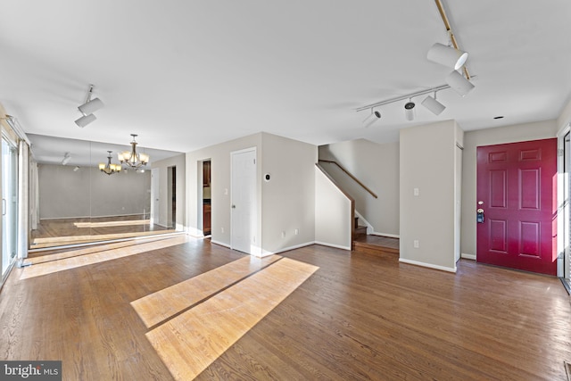 unfurnished living room featuring dark wood-type flooring, rail lighting, and an inviting chandelier